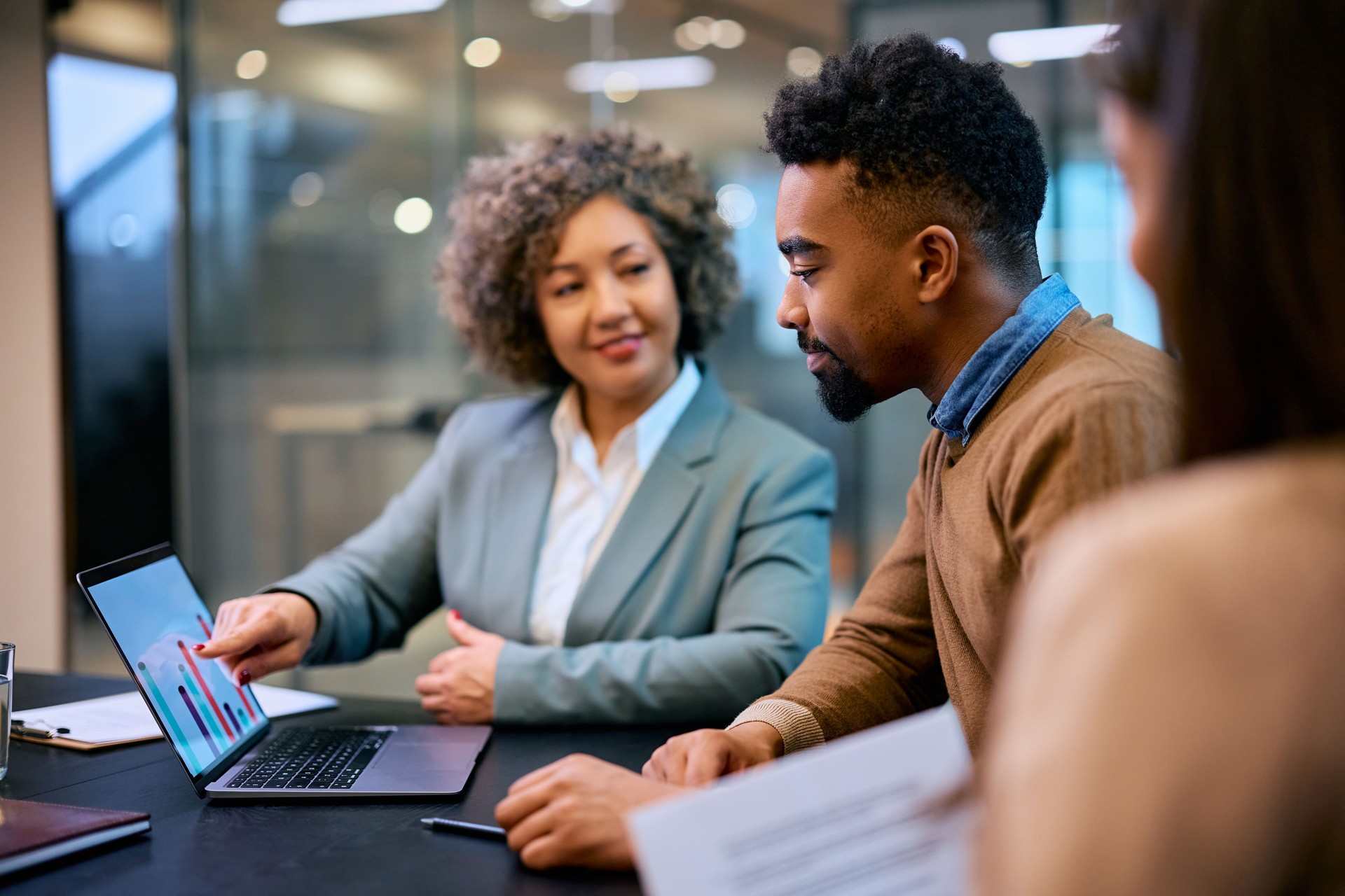 Smiling black man and financial consultant analyzing his investments on laptop in the office.