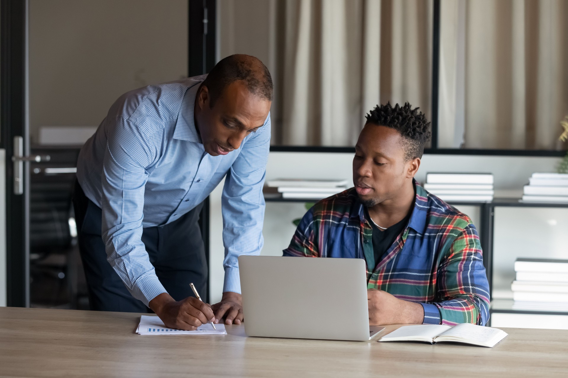 Serious African American adult mentor training intern at laptop